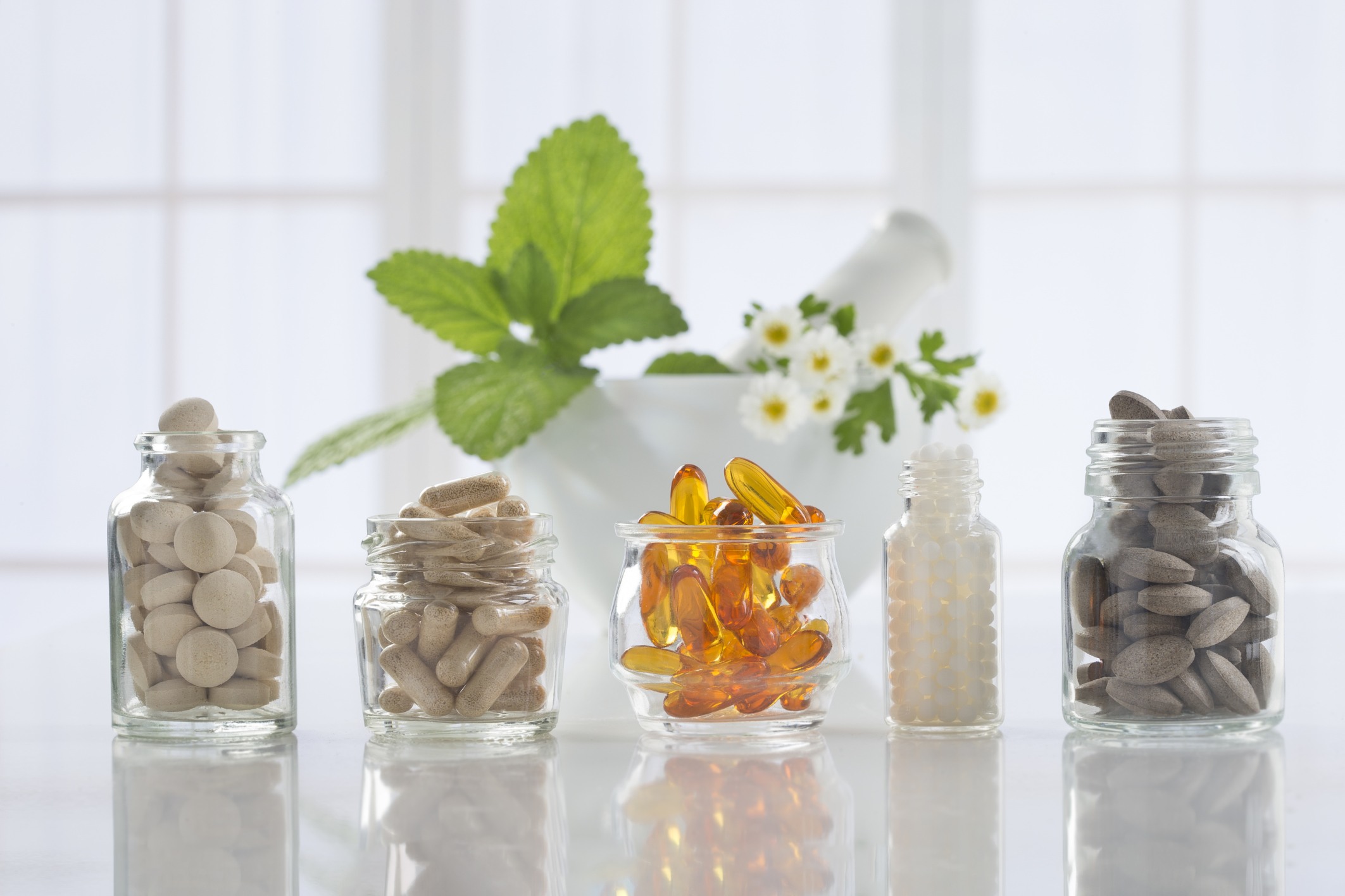 Softgels, capsules and tablets in glass bottles with fresh botanical ingredients